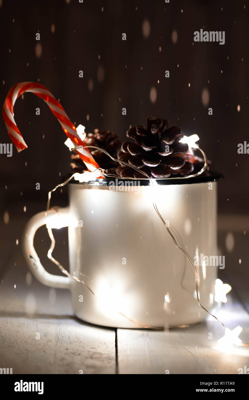 Tannenzapfen in Zinn Glas mit funkelnden sternförmige Garland und einzelne Zuckerstange stick. Weihnachtsschmuck. Dark Photo. Fallenden Schnee Effekt. Stockfoto