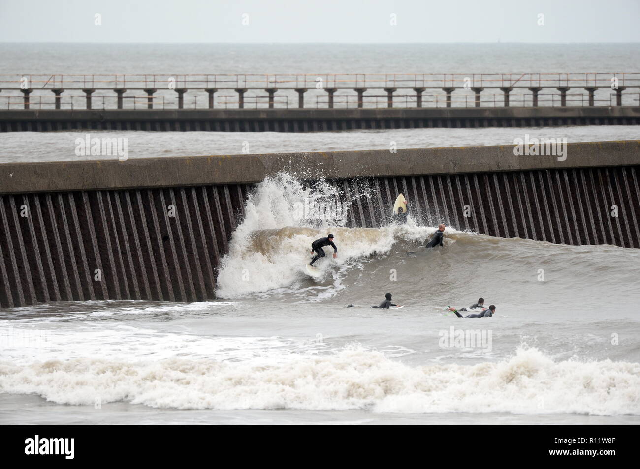 Surfen eine 'Man Made"-Welle aus einem Hafen Wand in Swansea Bay in der Nähe des Lage der vorgeschlagenen Gezeitenkraftwerk eine Gruppe Surfer warten Stockfoto
