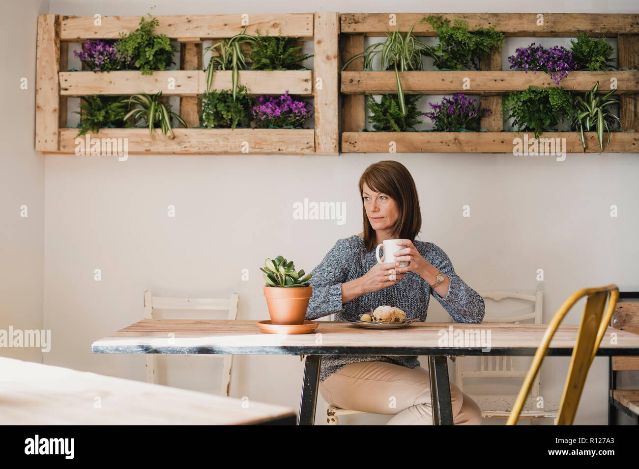 Reife Frau an einem Tisch sitzen in einem kleinen Café bei einer Tasse Kaffee. Sie schauen aus dem Fenster und genießen die Ruhe. Stockfoto