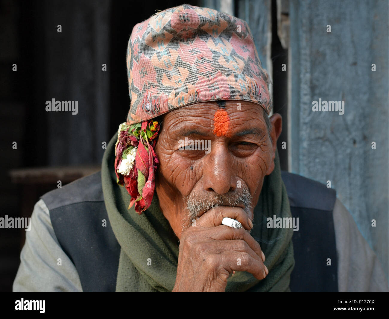 Ältere Nepali Newari Mann mit rotem tilaka Markierung auf seiner Stirn trägt den traditionellen nepalesischen Dhaka topi hat und raucht eine Zigarette. Stockfoto
