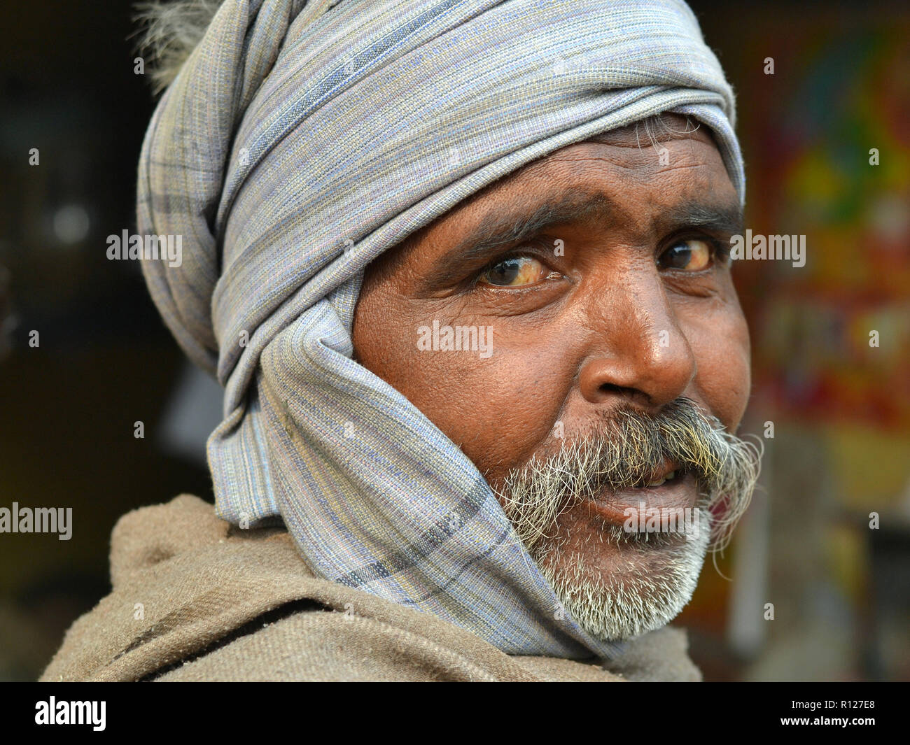 Indische Mann mit einem grauen Schnurrbart und gefühlvollen Augen trägt einen grauen wollenen Shawl über seinen Kopf im Winter kalt. Stockfoto