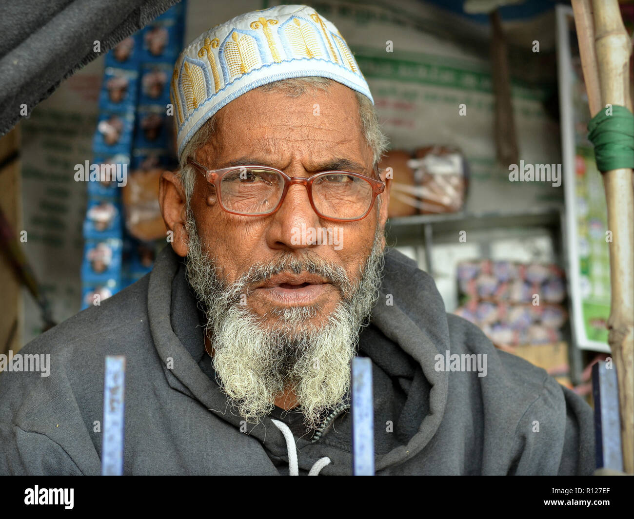 Älteren Indischen muslimischen Mann mit einem grauen Islamischen Bart und Brille trägt eine gestickte Islamischen Schädelkappe (taqiyah) und sieht in die Kamera. Stockfoto