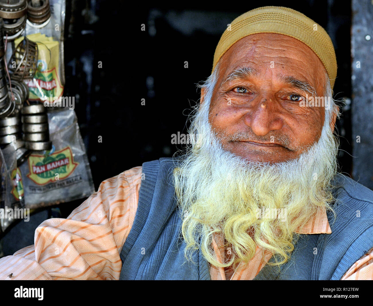 Alten Indischen muslimischen Mann mit einem weißen, langen und buschigen Vollbart, trägt einen gestrickten Senf-gelb Islamischen Schädelkappe (taqiyah) und posiert für die Kamera. Stockfoto