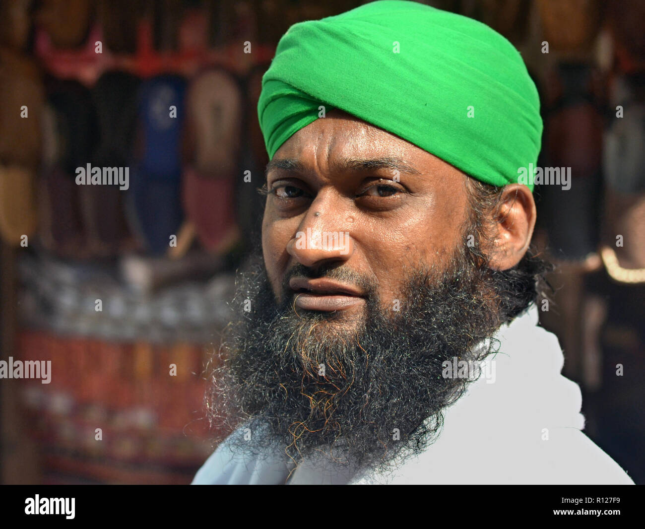 Afghani Schuh Kaufmann mit schwarzen Islamischen Bart trägt einen Turban-Stil Kopfschmuck in Grün und posiert für die Kamera. Stockfoto