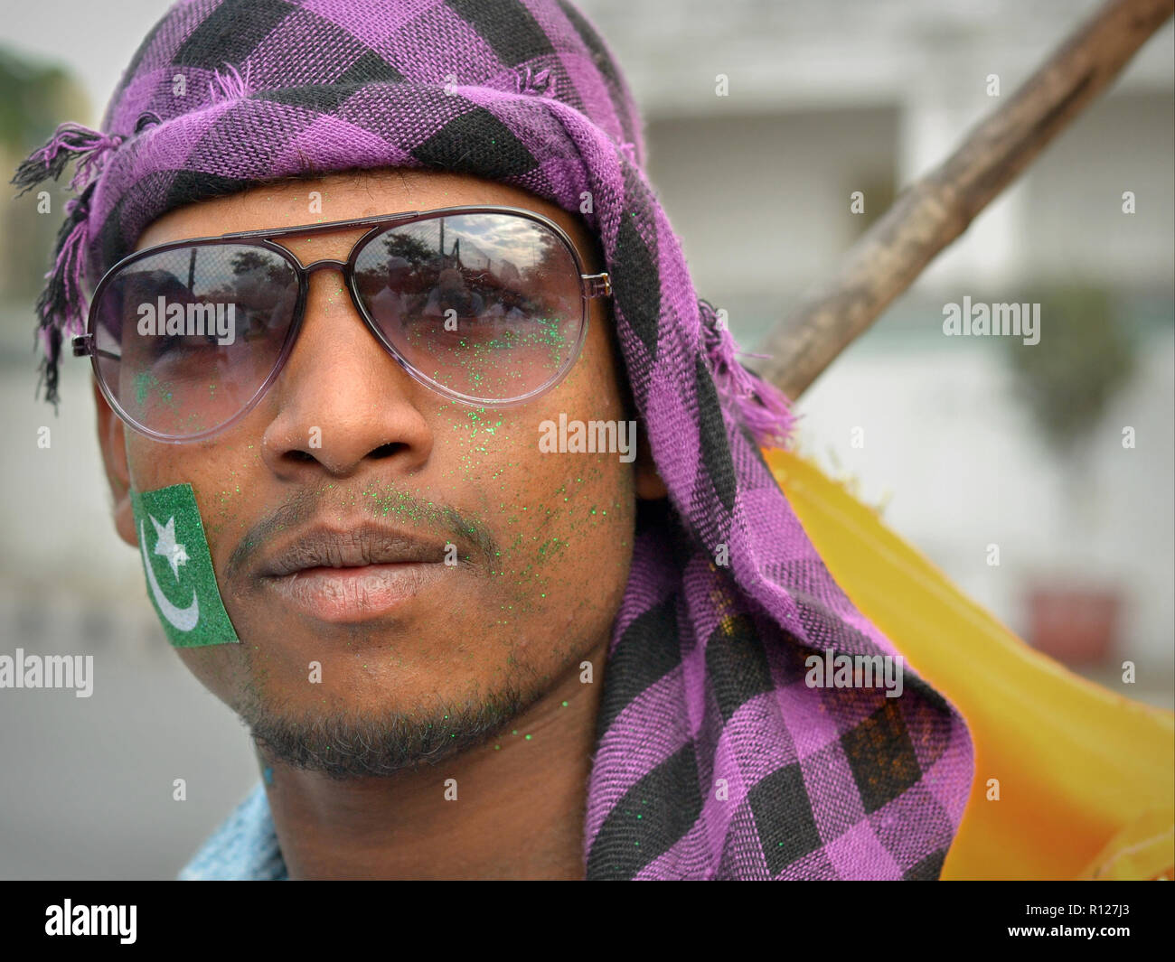 Junge Indische muslimische Mann mit grünem Glitter auf seine Wangen trägt aviator Sonnenbrille und einem karierten Kopftuch, während der Rabi' al-Awwal Festlichkeiten. Stockfoto