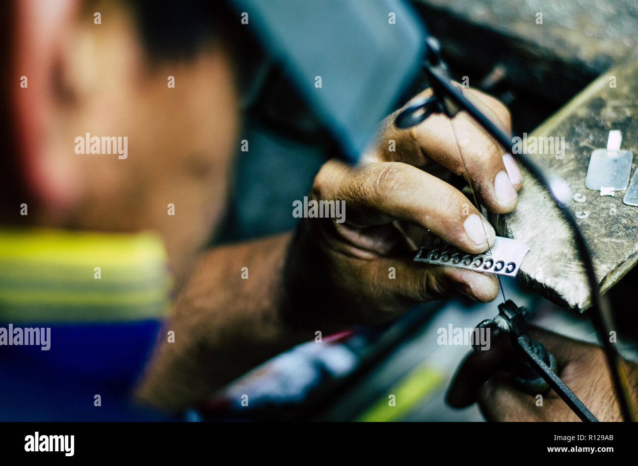 Hände Goldschmiedearbeiten des Menschen auf ein Stück Silber mit einer Metallsäge auf dem Arbeitstisch, Nahaufnahme, ausgewählte konzentrieren, enge Tiefenschärfe Stockfoto