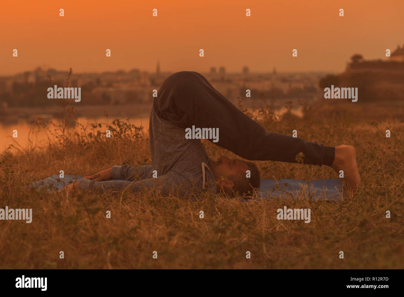 Man Yoga auf Sonnenuntergang mit Blick auf die Stadt, halasana/Pflug darstellen. Stockfoto