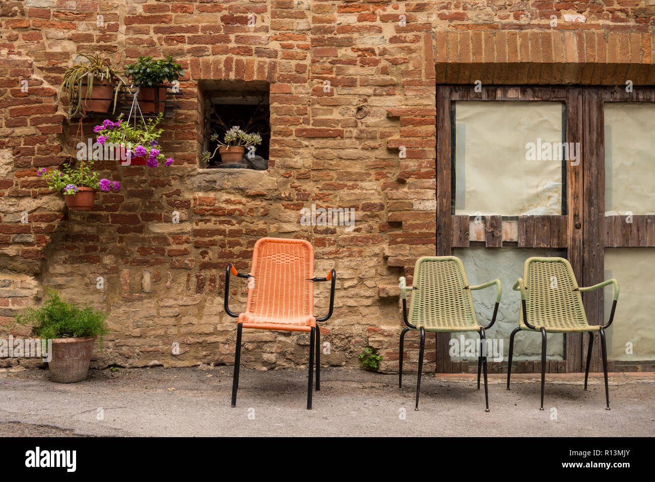 Drei bunten Stühlen links außerhalb von einem alten Backsteingebäude, Chiusure, einem kleinen Dorf in der Provinz von Siena, Toskana, Italien Stockfoto