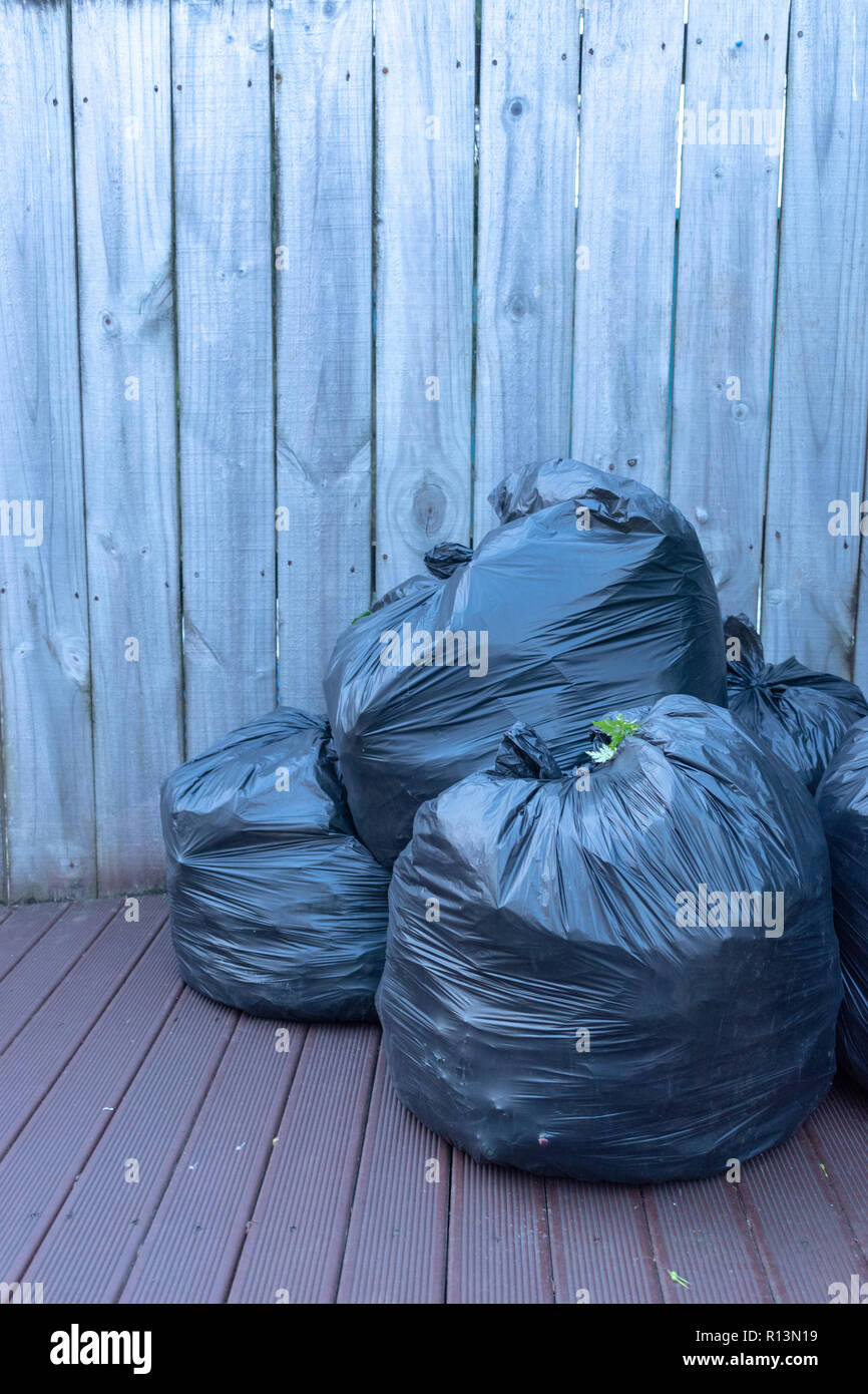 Vertikale Bild von drei schwarzen Kunststoff Abfallsäcke verpackt und auf dem Deck gegen einen Holzzaun zu nehmen Stockfoto