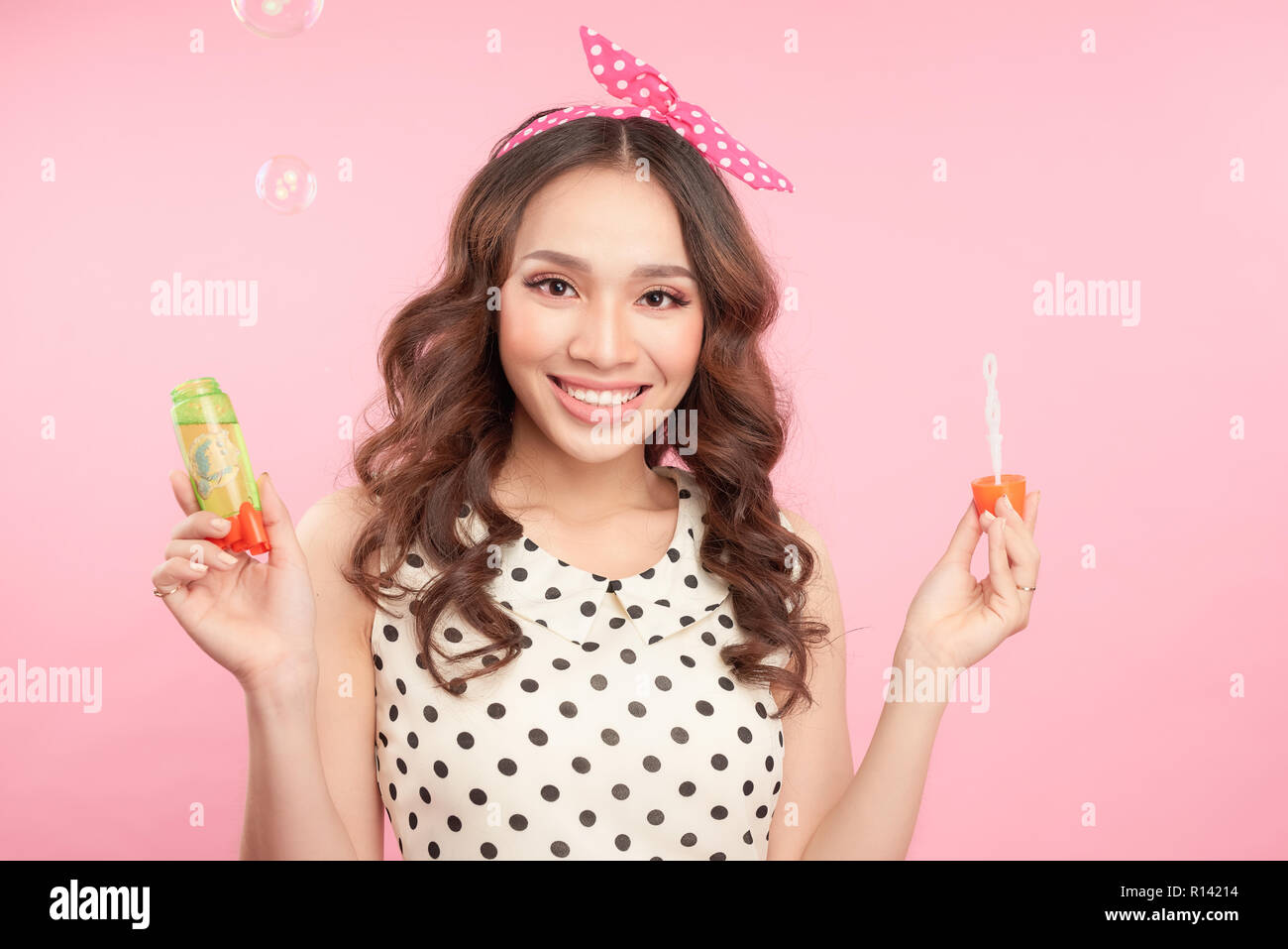 Verspielte Frau, Blasen, Blasen in die Kamera wie Sie feiert eine besondere Gelegenheit oder Geburtstag, über rosa Hintergrund Stockfoto