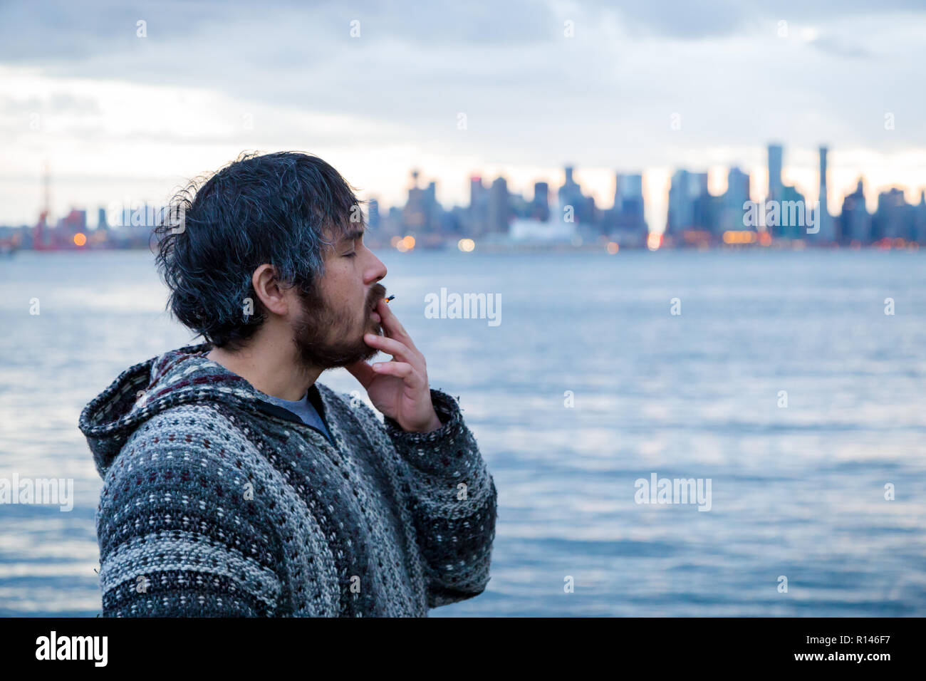 Ein junger Mann rauchen eine gemeinsame mit der Innenstadt von Vancouver, BC, im Hintergrund kurz nach Kanadische Marihuana Legalisierung. Stockfoto