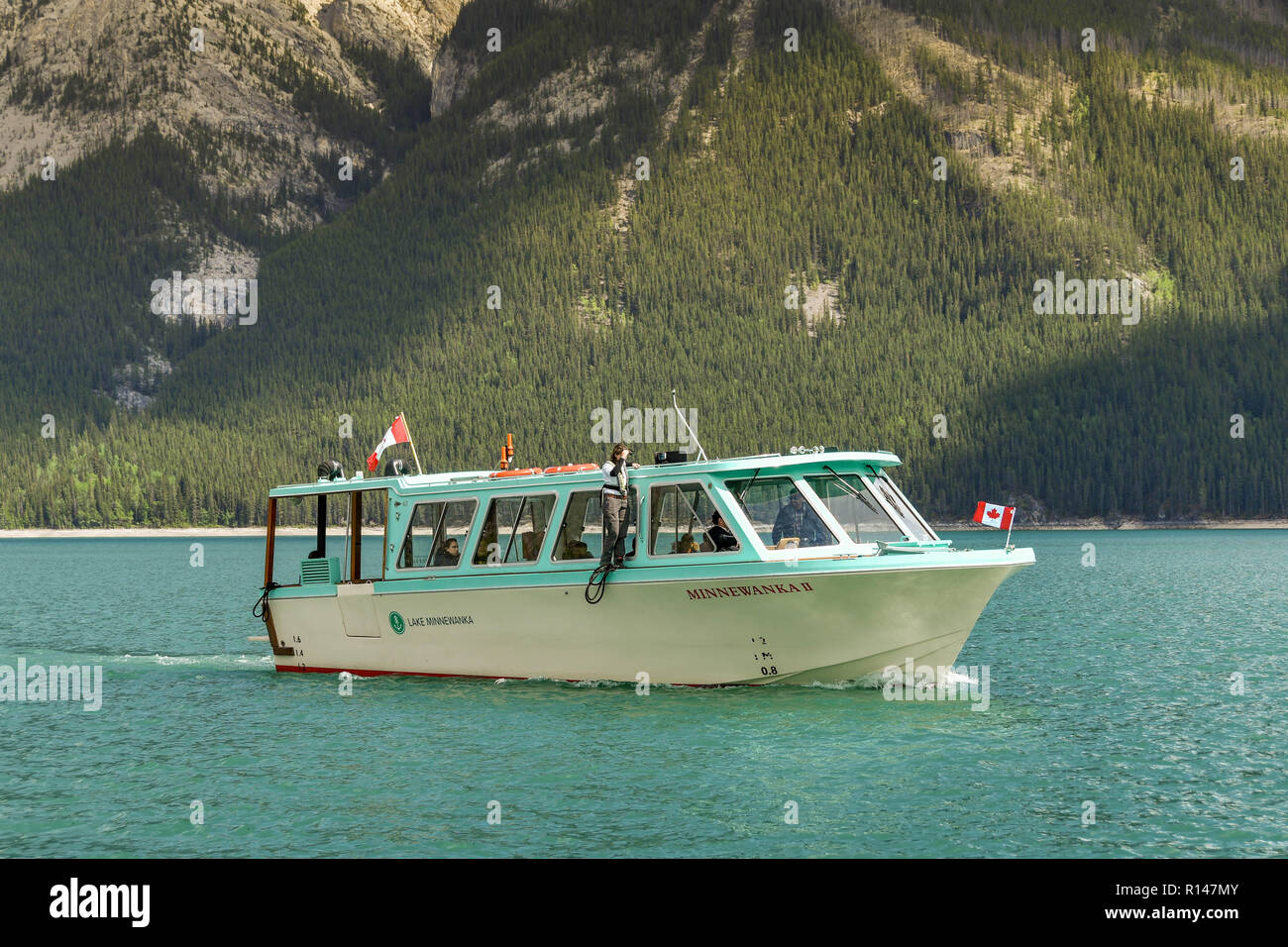 BANFF, AB, Kanada - Juni 2018: Malerische Aussicht auf eine kleine touristische Sehenswürdigkeiten Boot auf Lake Minnewanka in der Nähe von Banff. Ein Mitglied der Crew steht auf der Stockfoto