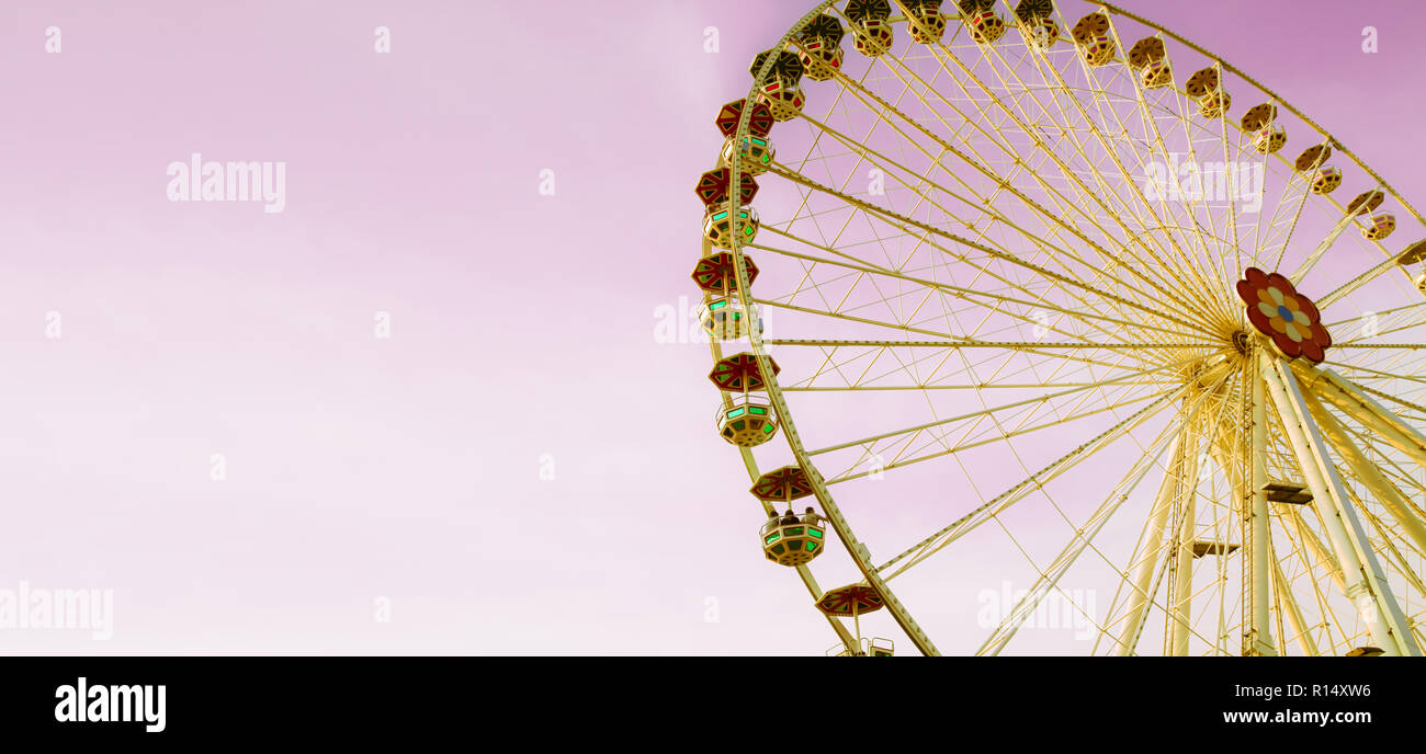Riesenrad (oder Rad Wunder) in einem Freizeitpark an einem sonnigen Tag mit rosa Himmel. Foto Farbe getönt für Vintage Retro Look mit gelben Farbtönen gehalten und mit hellen Stockfoto