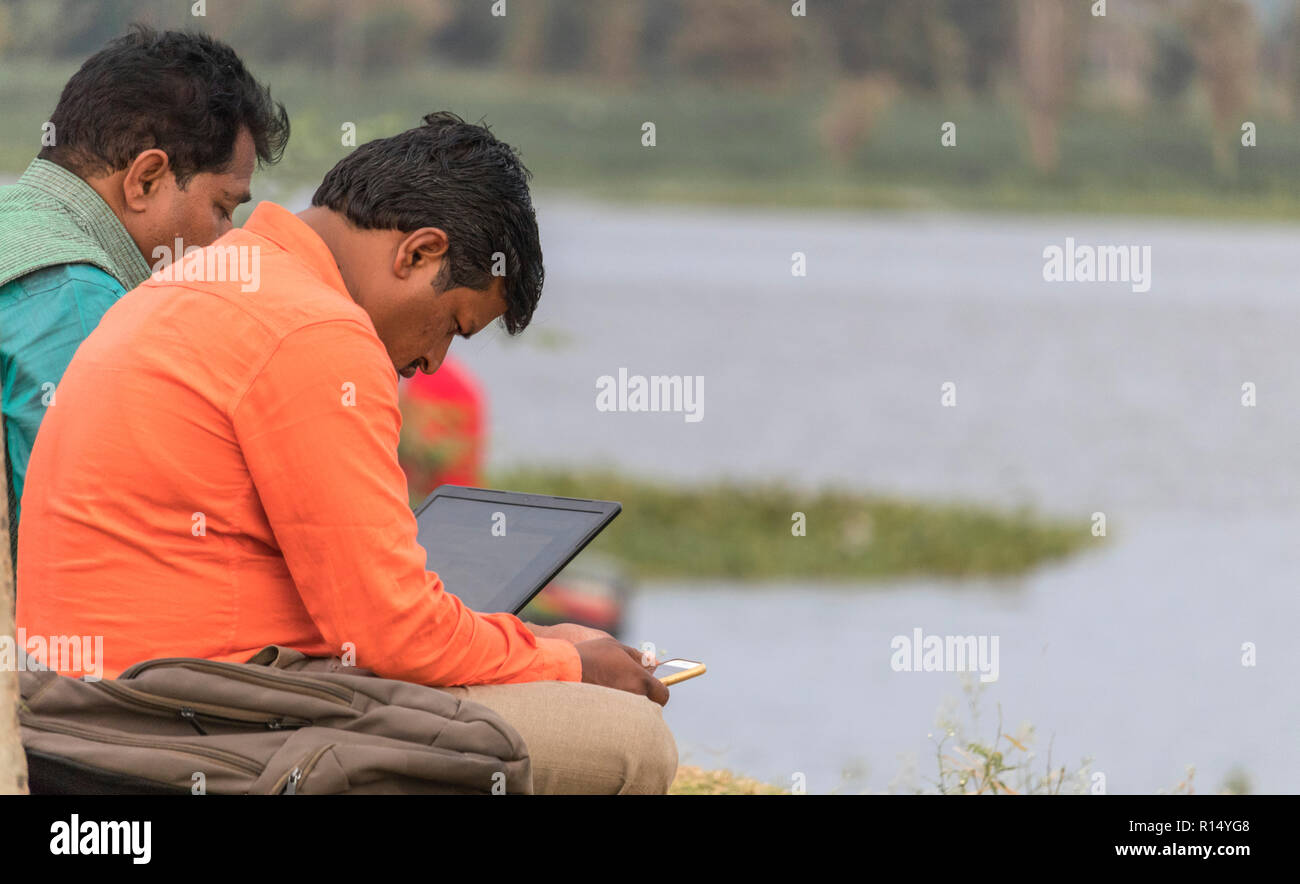 Mann bei der Arbeit am Laptop im Freien in Seeblick Kamalapur, Phantasialand, Karnataka, Indien sitzen Stockfoto