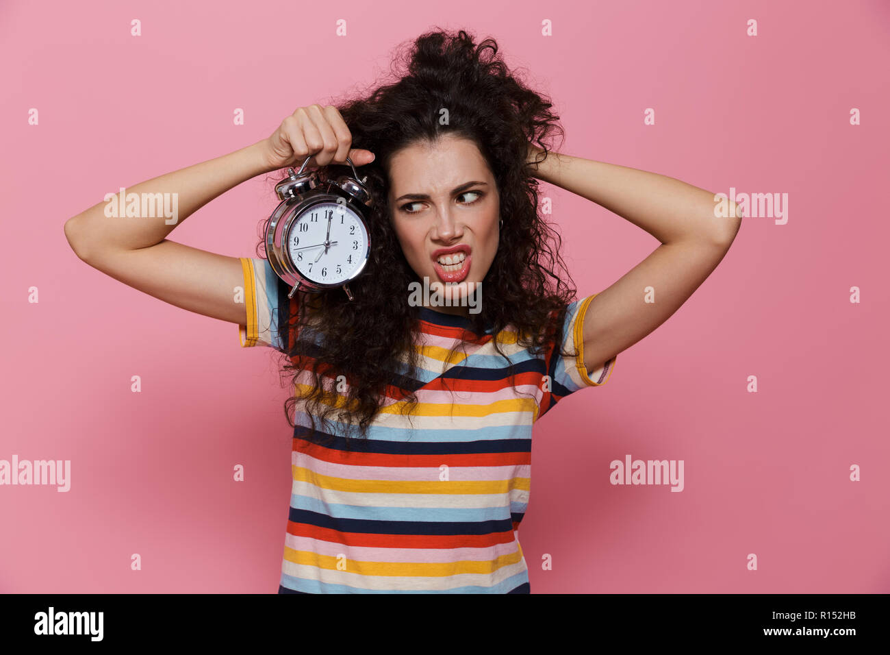 Foto von wütende Frau 20s mit lockigem Haar holding Wecker über rosa Hintergrund isoliert Stockfoto