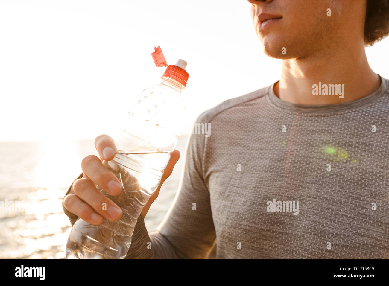Zugeschnittenes Bild von gutaussehenden jungen Sport Mann stand am Strand Trinkwasser. Stockfoto