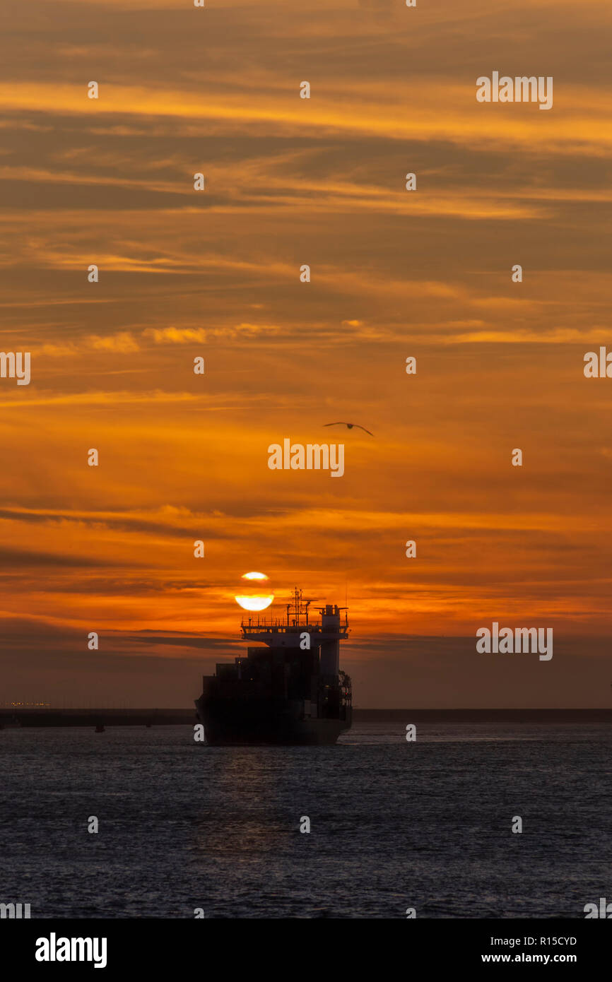 Container schiff Verlassen des Rotterdamer Hafen auf dem Weg zur tiefen Ozean unter einem leuchtenden Sonnenuntergang, Amsterdam, Niederlande Stockfoto