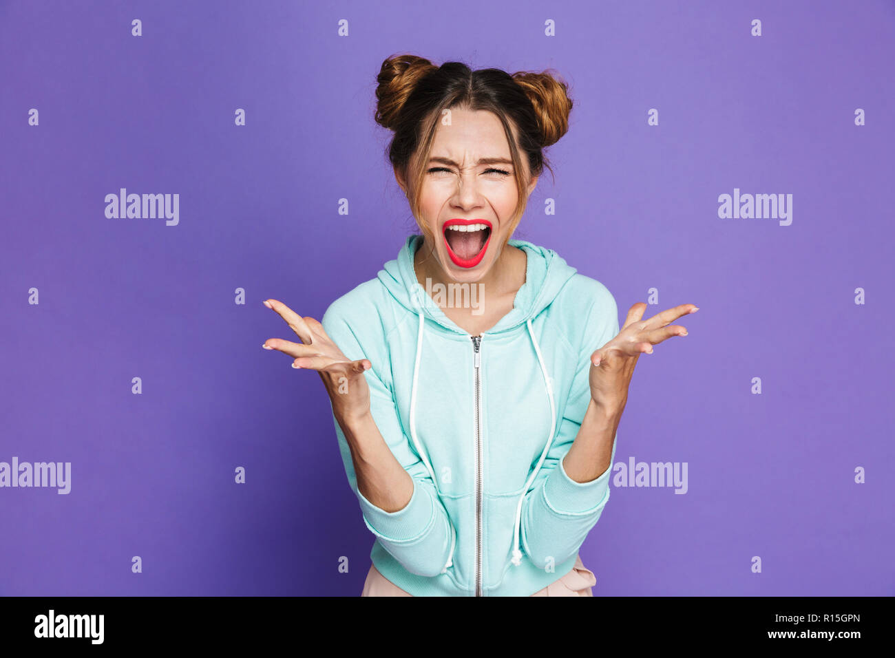 Portrait von wütenden Frau mit zwei Brötchen schreien und wirft die Hände über violette Hintergrund im Studio isoliert Stockfoto