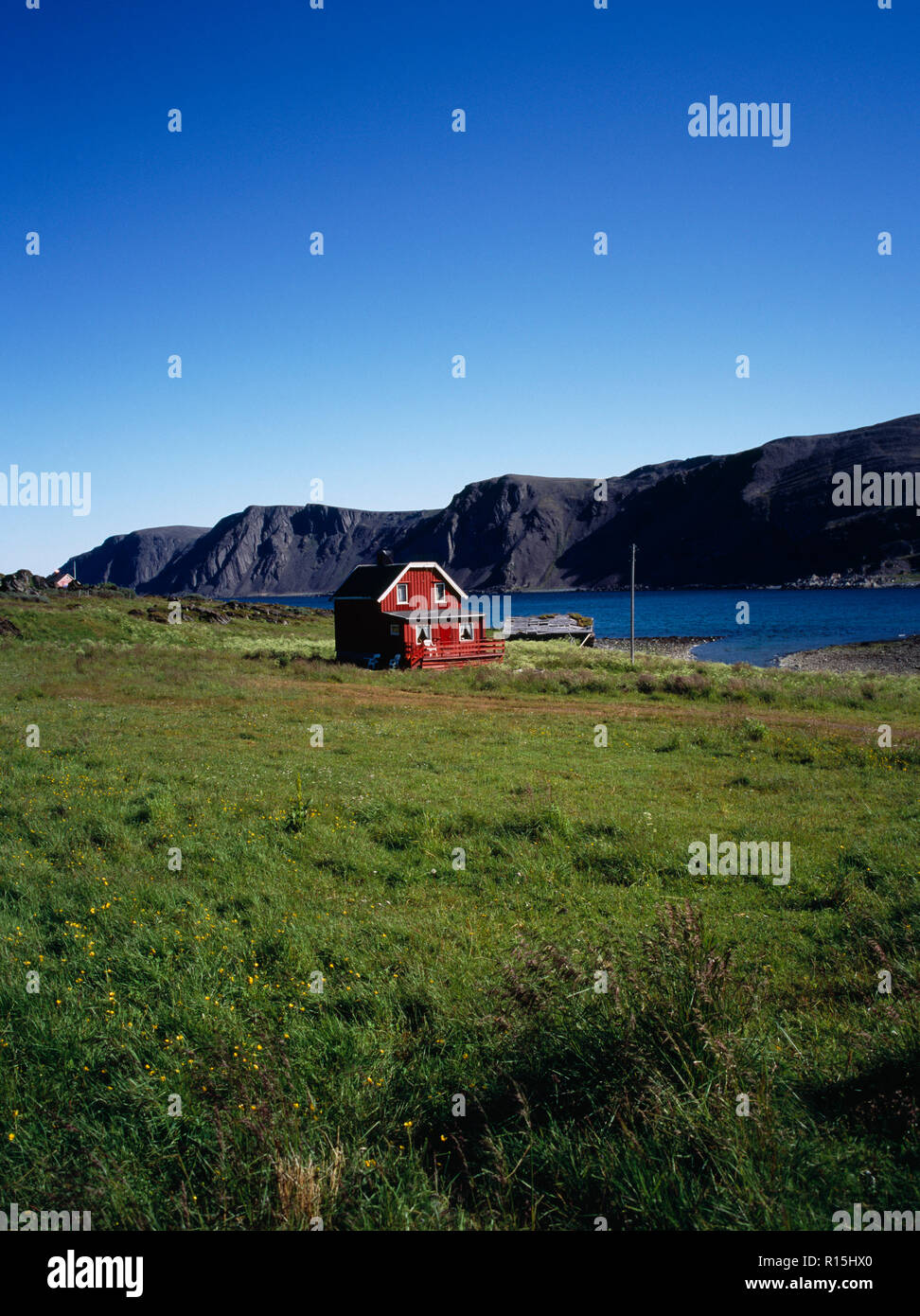 Norwegen, Finnmark, Nordkinnhalvoya, Rot lackiert Sommer Bauernhaus mit weiß lackierten Traufen und Fensterrahmen neben Sandfjorden in Bereich in tiefem Schnee im Winter abgedeckt. Stockfoto