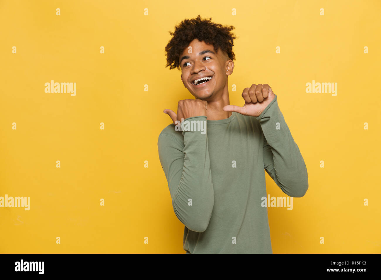 Portrait von jugendlich afrikanischen Kerl in stilvollen afro Frisur Pointing Finger rückwärts an Copyspace über Gelb Hintergrund isoliert Stockfoto