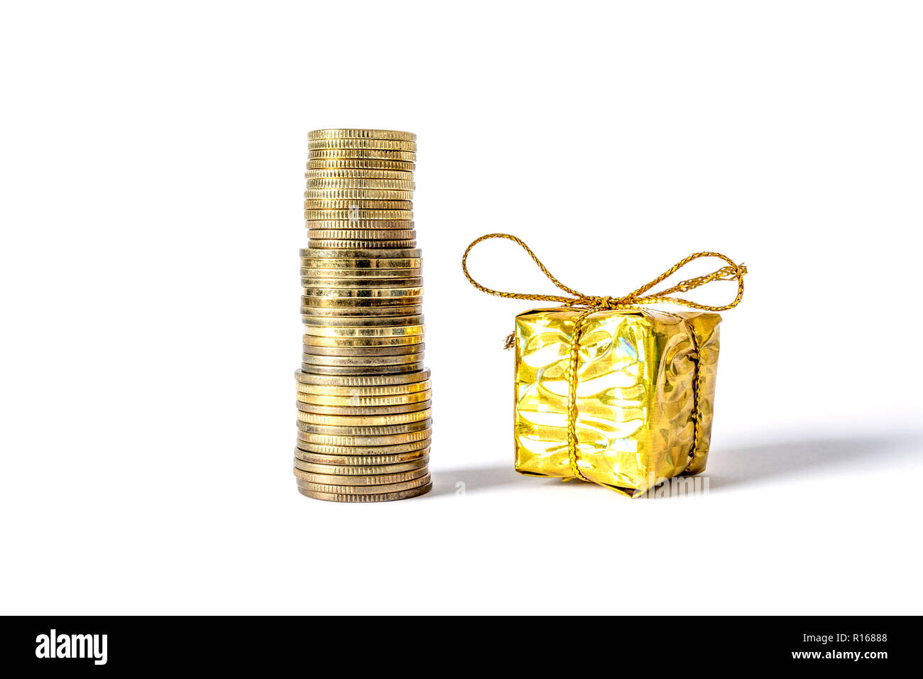 Geschenkbox in Gold Verpackung verband mit einem Bogen neben Münzen Spalte  close-up auf weißem Hintergrund Stockfotografie - Alamy