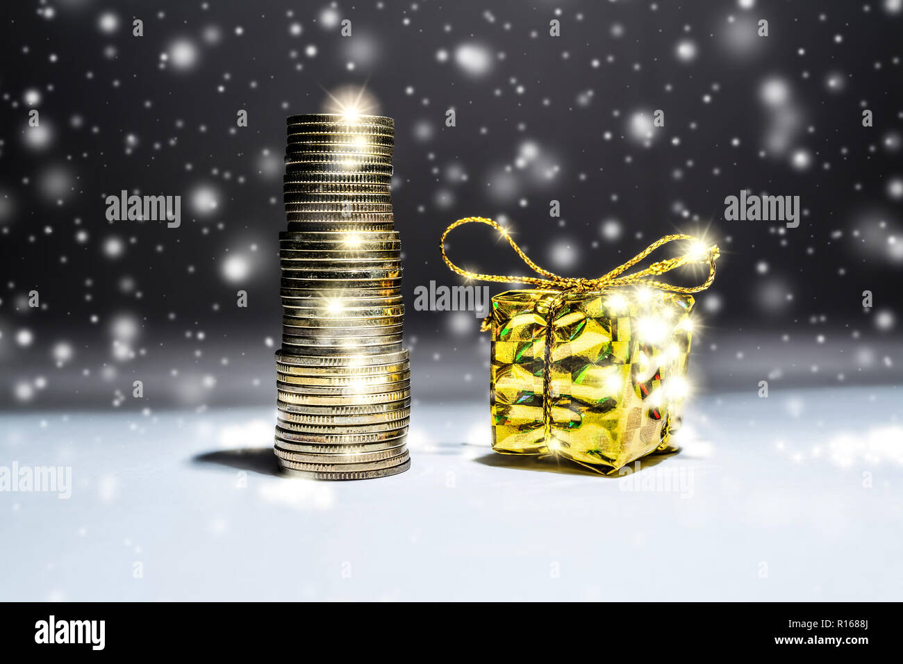 Das neue Jahr still-Leben mit einem Stapel von Goldmünzen und eine Box mit einem Geschenk auf einem dunklen Hintergrund mit fallendem Schnee Stockfoto