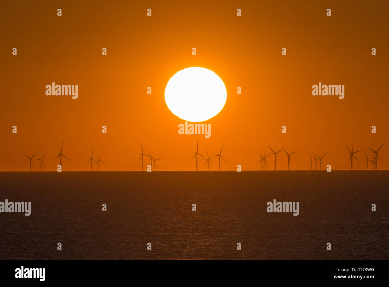 Sonnenuntergang über dem Meer mit Windkraftanlagen am Horizont Stockfoto