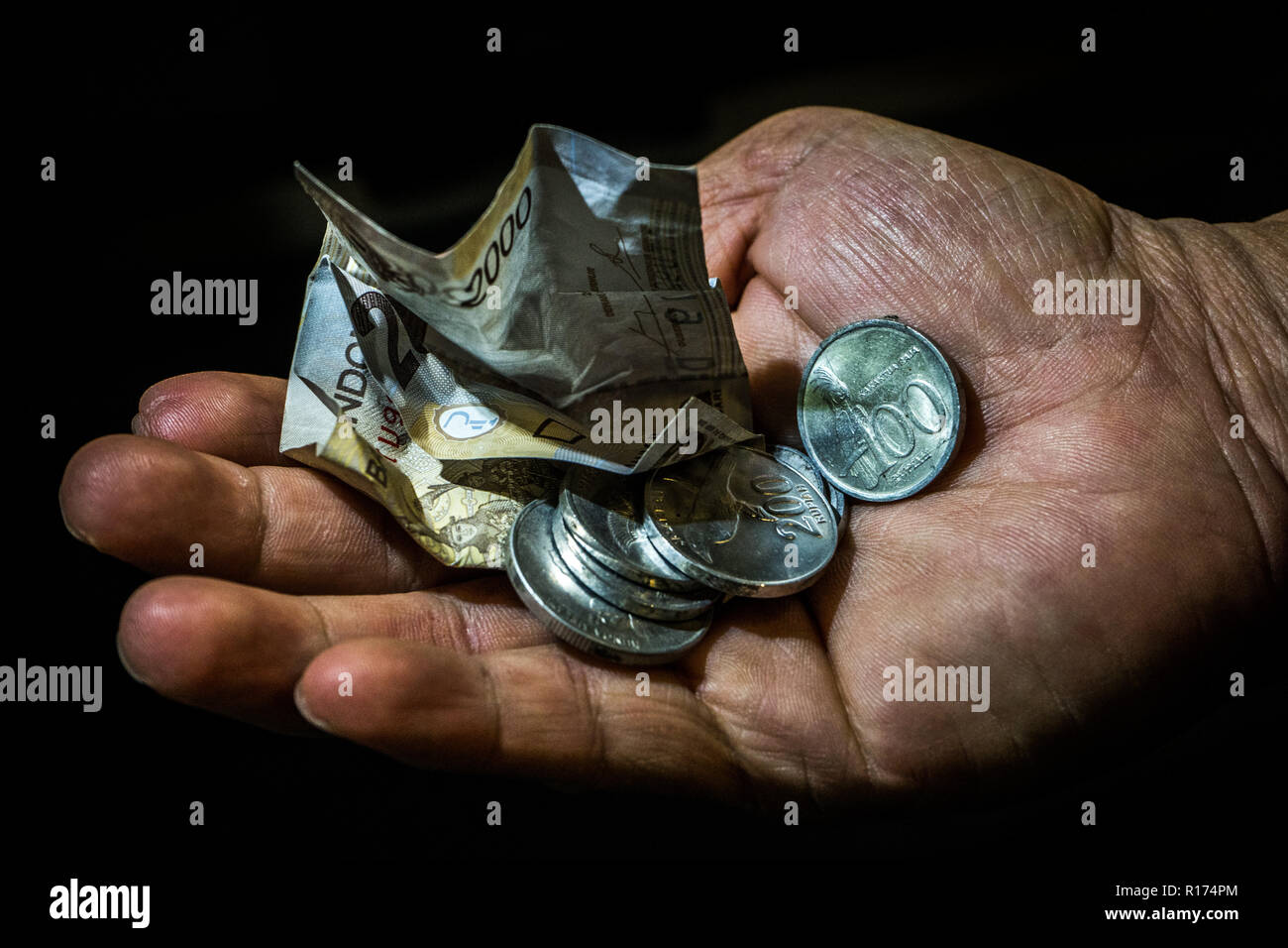 Indonesien, rupiah kleine Bill und Münzen in der Hand eines asiatischen Person isoliert. Konzept der Betteln für verlassen, schlechte Person. Stockfoto