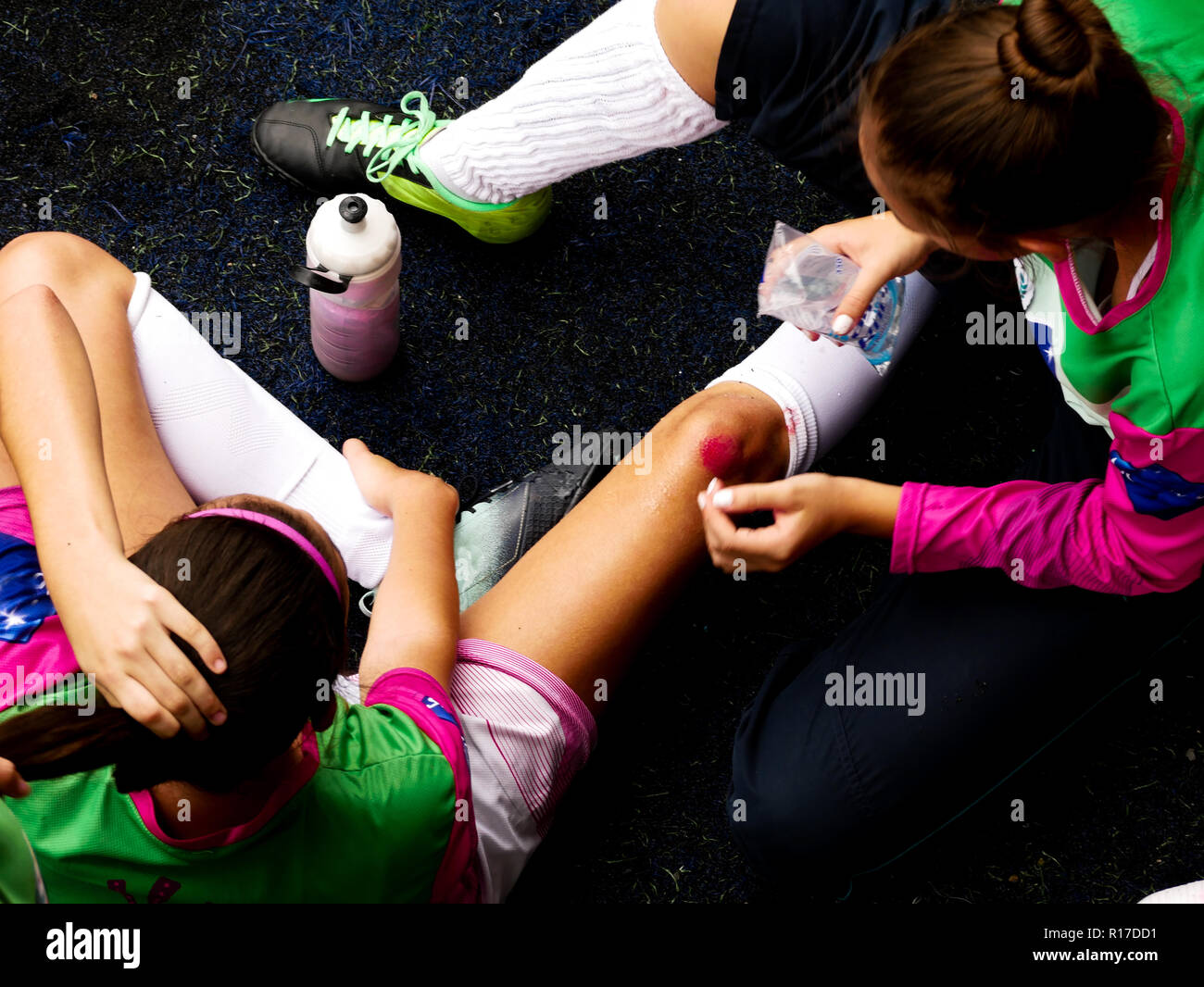 Ein torwart Mädchen mit lackierten Nägel Reinigung a Wounded Knee team Mate mit Wasser während eines Fußball-Spiels auf einem Kunstrasen Feld. Stockfoto