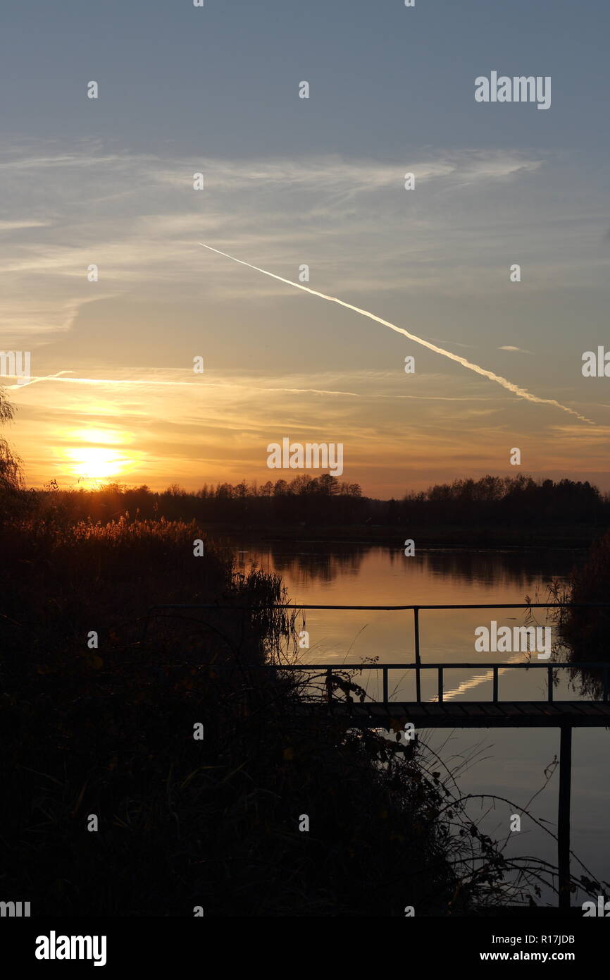 Fußgängerbrücke über Strom fließt in den See bei Sonnenuntergang im Herbst Stockfoto