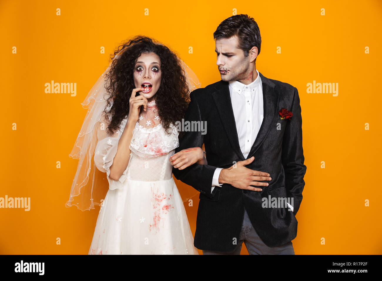 Foto der jungen Zombie paar Bräutigam und Braut mit einem Hochzeitskleid Outfit und Halloween Make-up von der Kamera über Gelb Hintergrund suchen Stockfoto