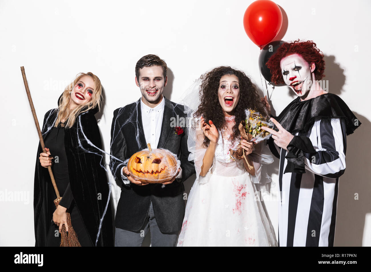 Gruppe von Lachen Freunde in gruselige Kostüme feiern Halloween gekleidet isoliert auf weißem Hintergrund, Luftballons, gebogene Kürbis, Besen Stockfoto