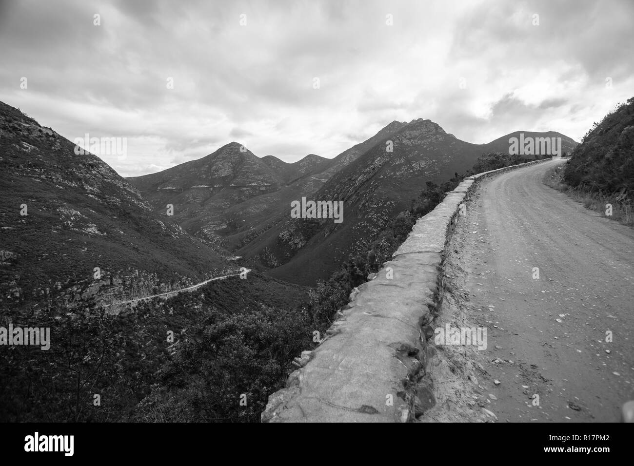 Hohe robuste Alte unbefestigte Straße durch schroffe Berge in schwarzen und weißen Landschaft. Stockfoto