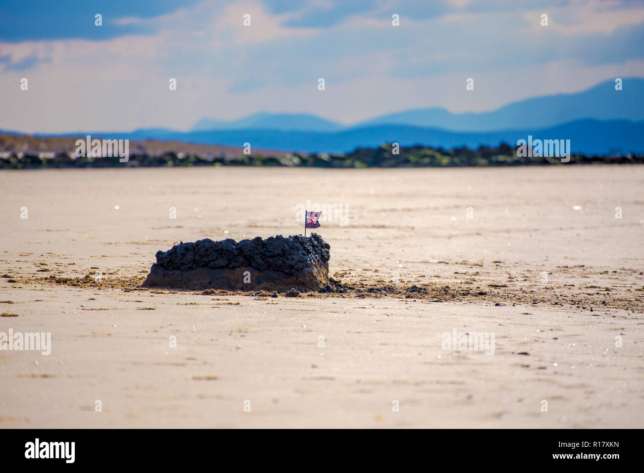 Sand Castle/Schlamm Burg gekrönt mit einem kleinen Schädel & Totenkopf Flagge am Strand. Die Berge von Snowdoncan im Hintergrund gesehen werden. Prestatyn, noch Stockfoto