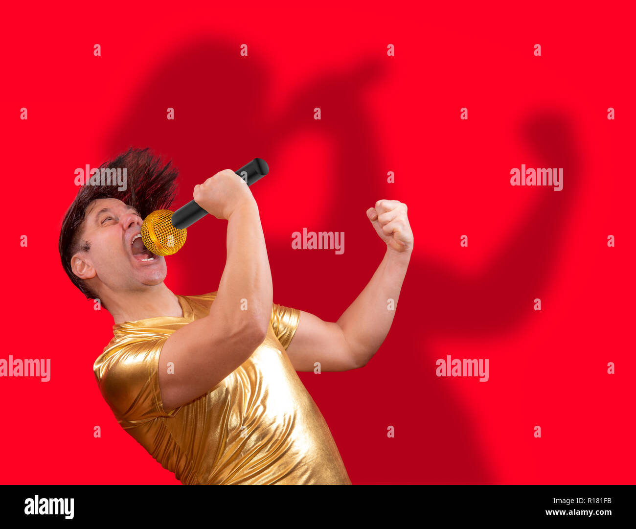 Die angeregten Sänger mit einem Mikrofon mit eigenen Schatten auf rotem Hintergrund. Crazy emotionale Mann in Golden Shirt singen auf Mic. Stockfoto