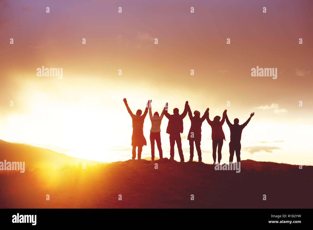 Große Gruppe der glückliche Freunde mit erhobenen Händen bei Sonnenuntergang. Die Silhouetten. Einheit, Erfolg, Team oder Freundschaft Konzept Stockfoto