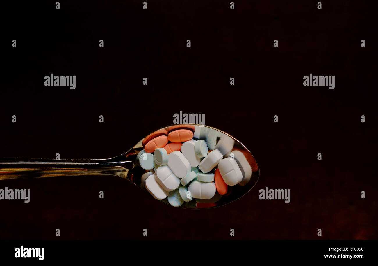 Closeup Bild einer Menge der Droge Pillen in Edelstahl Löffel über dunkles braun Holz- Hintergrund, zu viele Drogen Konzept Stockfoto