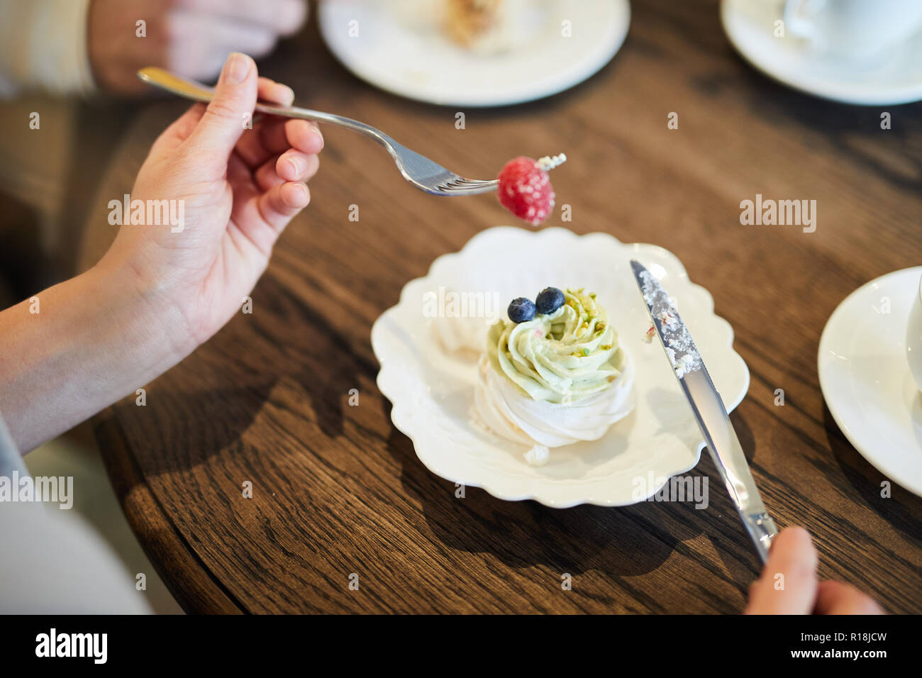 Reif lecker Himbeeren auf Messer und Gabel von jungen weiblichen statt über Platte mit cremiger Cupcake Stockfoto