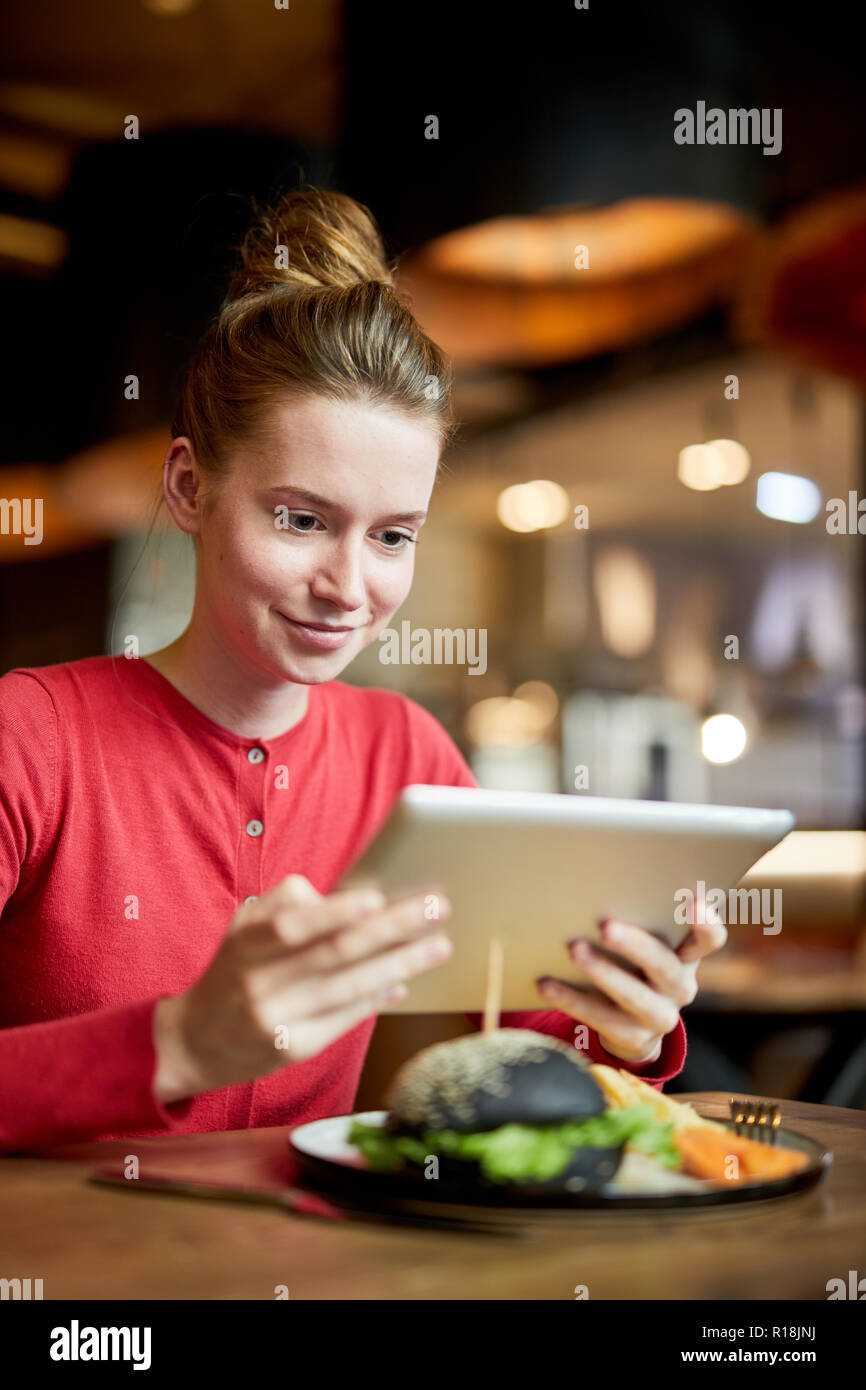 Hübsches Mädchen mit Touchpad sitzen durch serviert Tabelle in ein Café und beobachten, Film oder Video im Netz Stockfoto