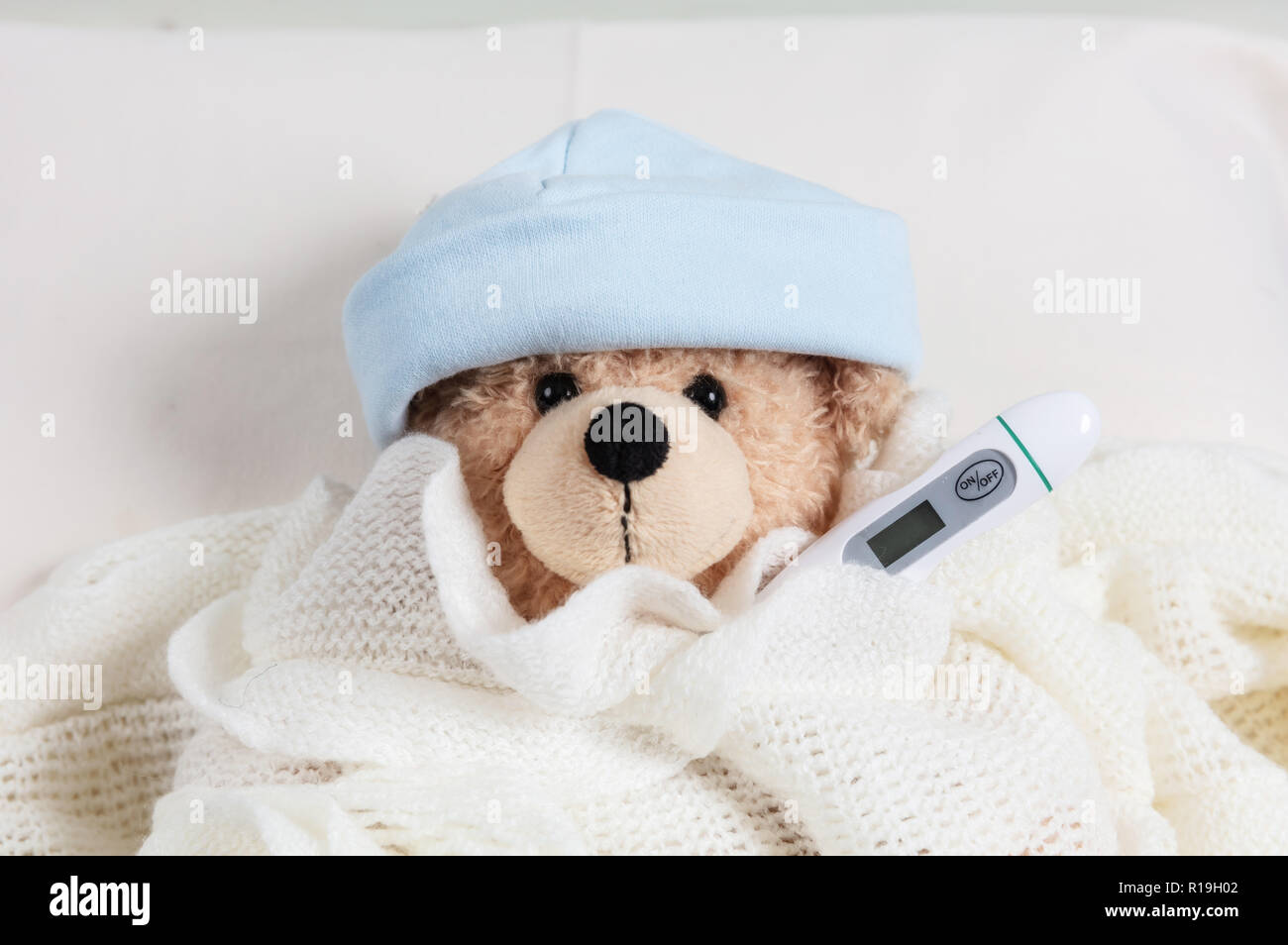 Fieber, Erkältung, Rauchgas Konzept. Cute Teddy Boy mit einem Thermometer im Bett, mit einer warmen Decke abgedeckt Stockfoto