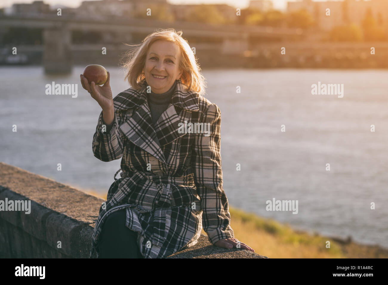 Ältere Frau genießt Apple essen, während Sie durch den Fluss sitzen. Stockfoto