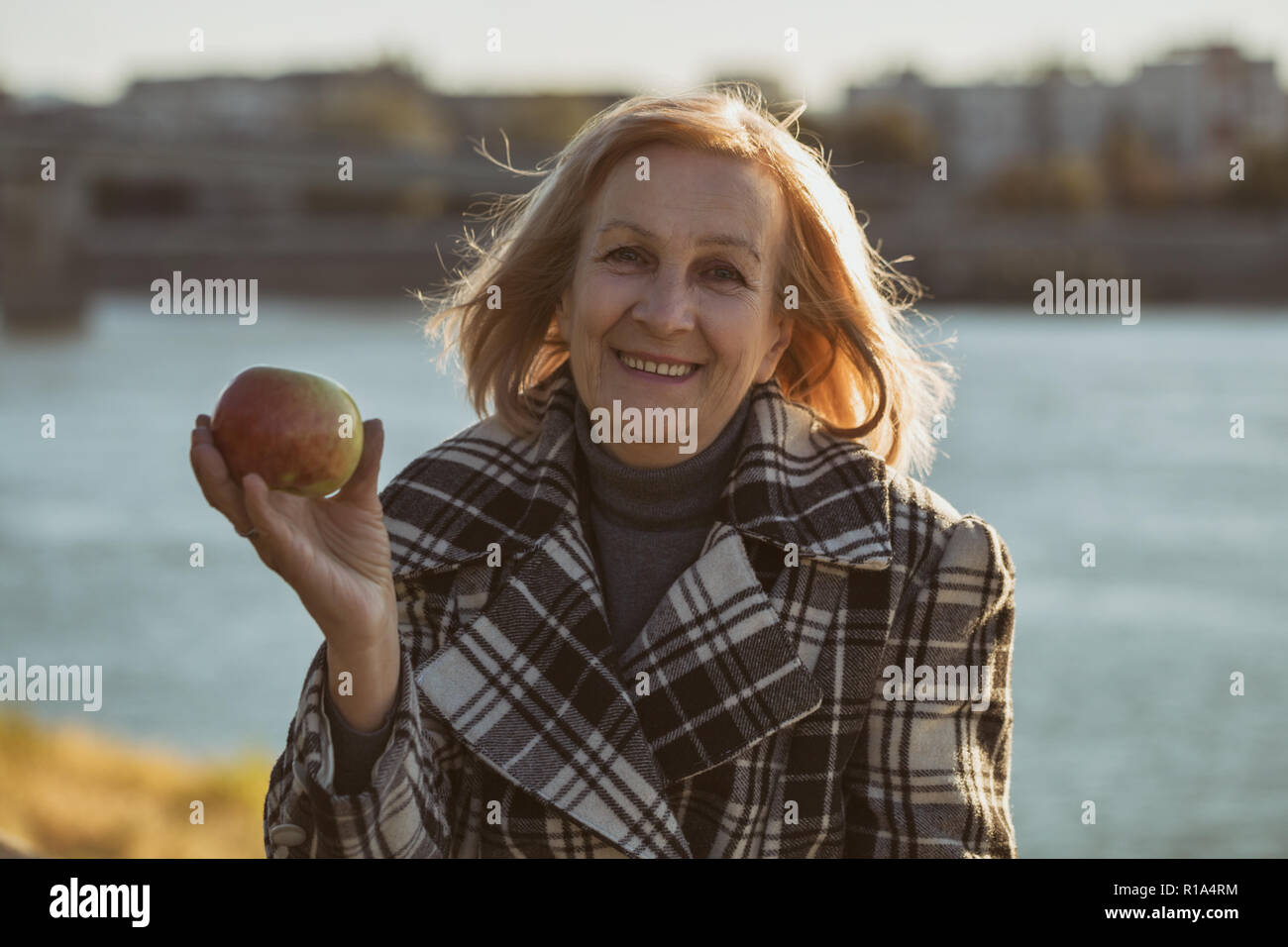 Ältere Frau genießt Apple essen, während Sie durch den Fluss sitzen. Stockfoto