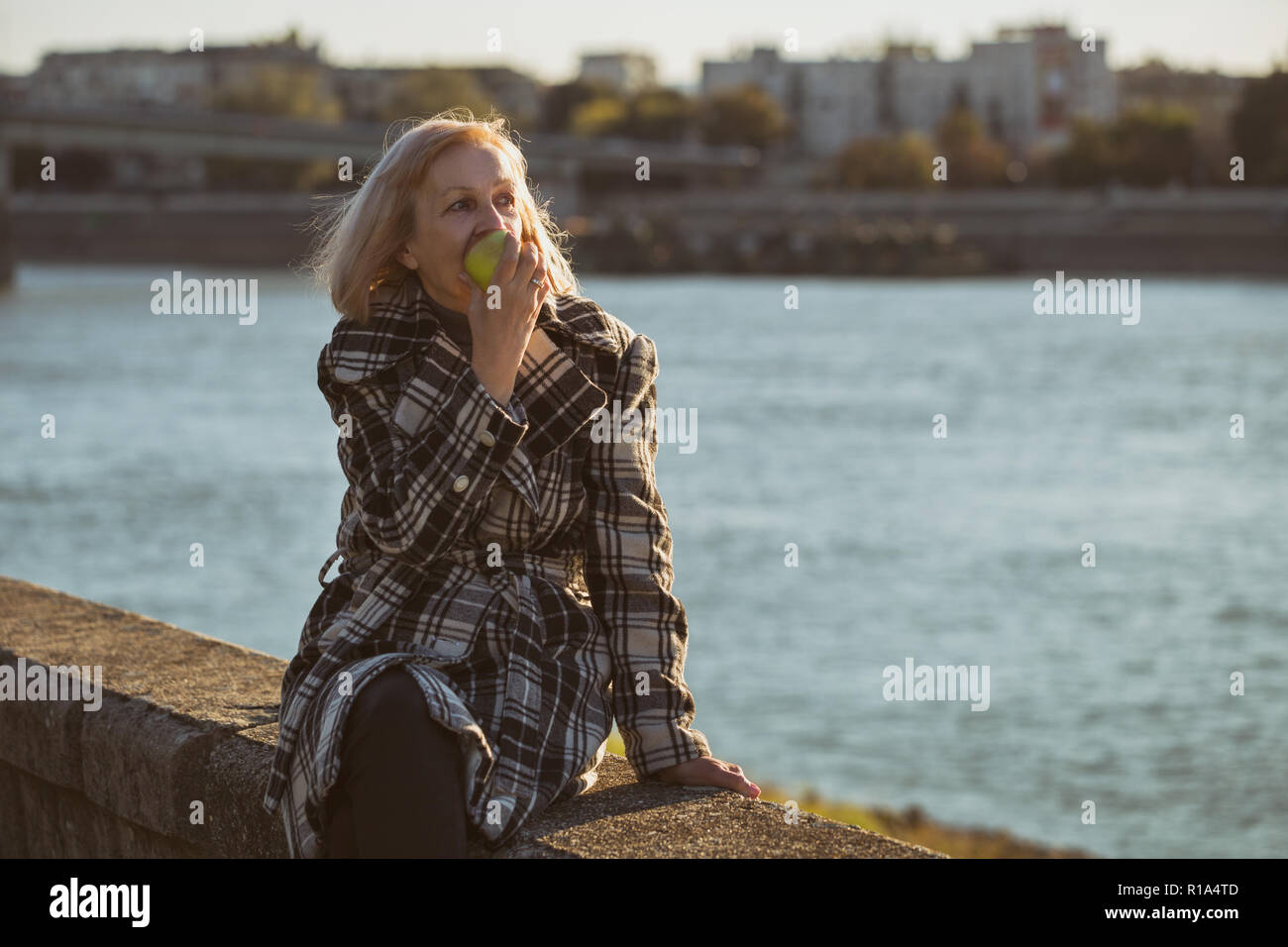 Ältere Frau genießt Apple essen, während Sie durch den Fluss sitzen. Stockfoto