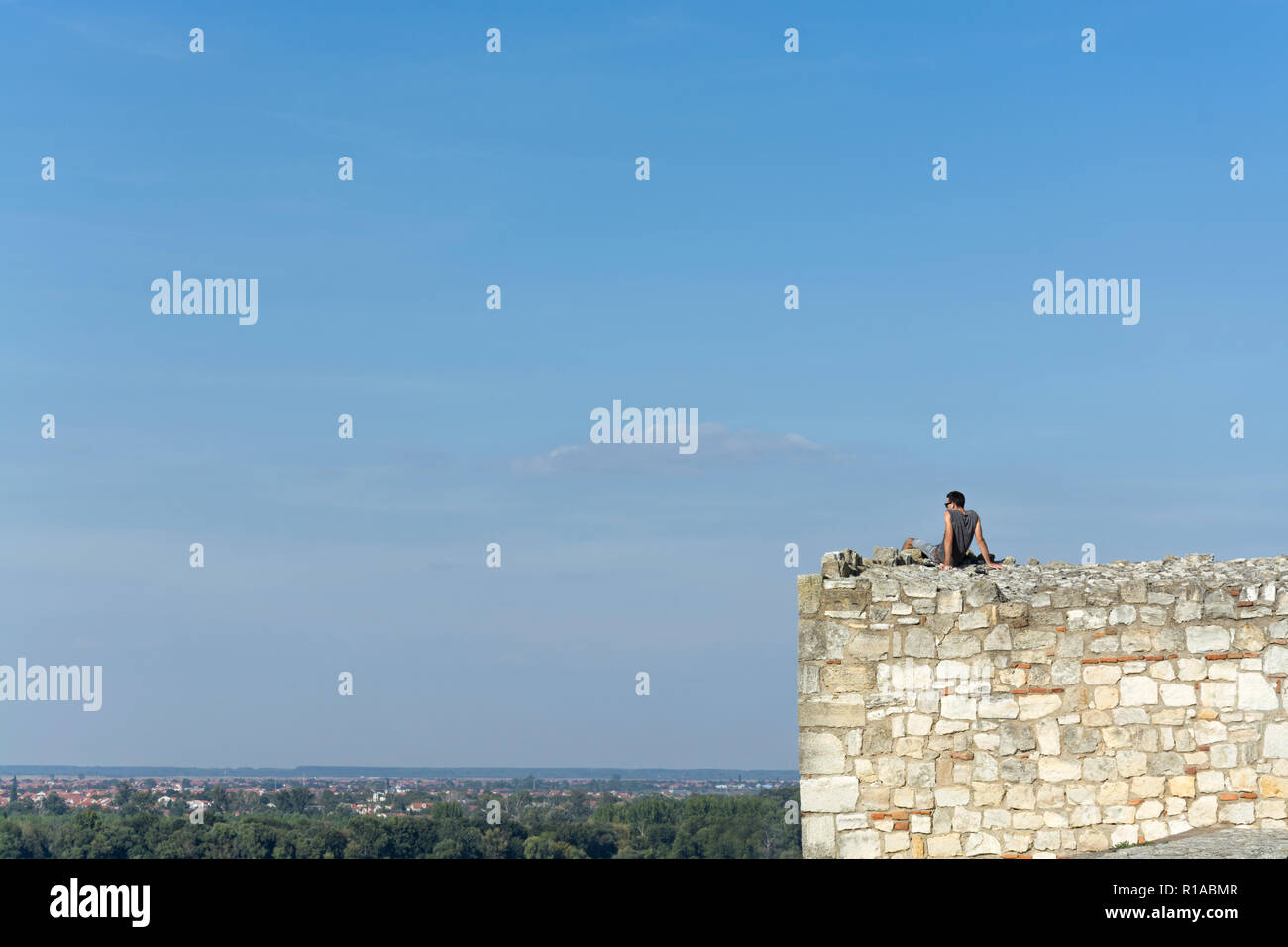 Dunkelhaarige junge Mann mit Sonnenbrille und Ohrkissen beaufsichtigt das Stadtbild an einem hellen Sommertag von der steinernen Wachturm der Festung Kalemegdan in Bel Stockfoto