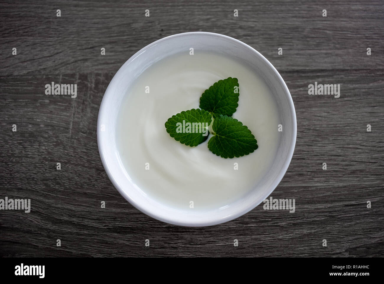 Keramische Schüssel mit weißen Joghurt und Minze auf dunklem Hintergrund von oben isoliert Stockfoto