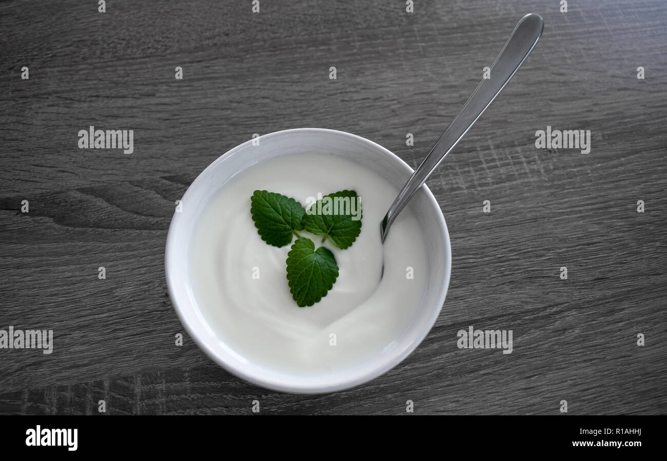 Keramische Schüssel mit weißen Joghurt, Minze und Löffel auf dunklem Hintergrund von oben isoliert Stockfoto