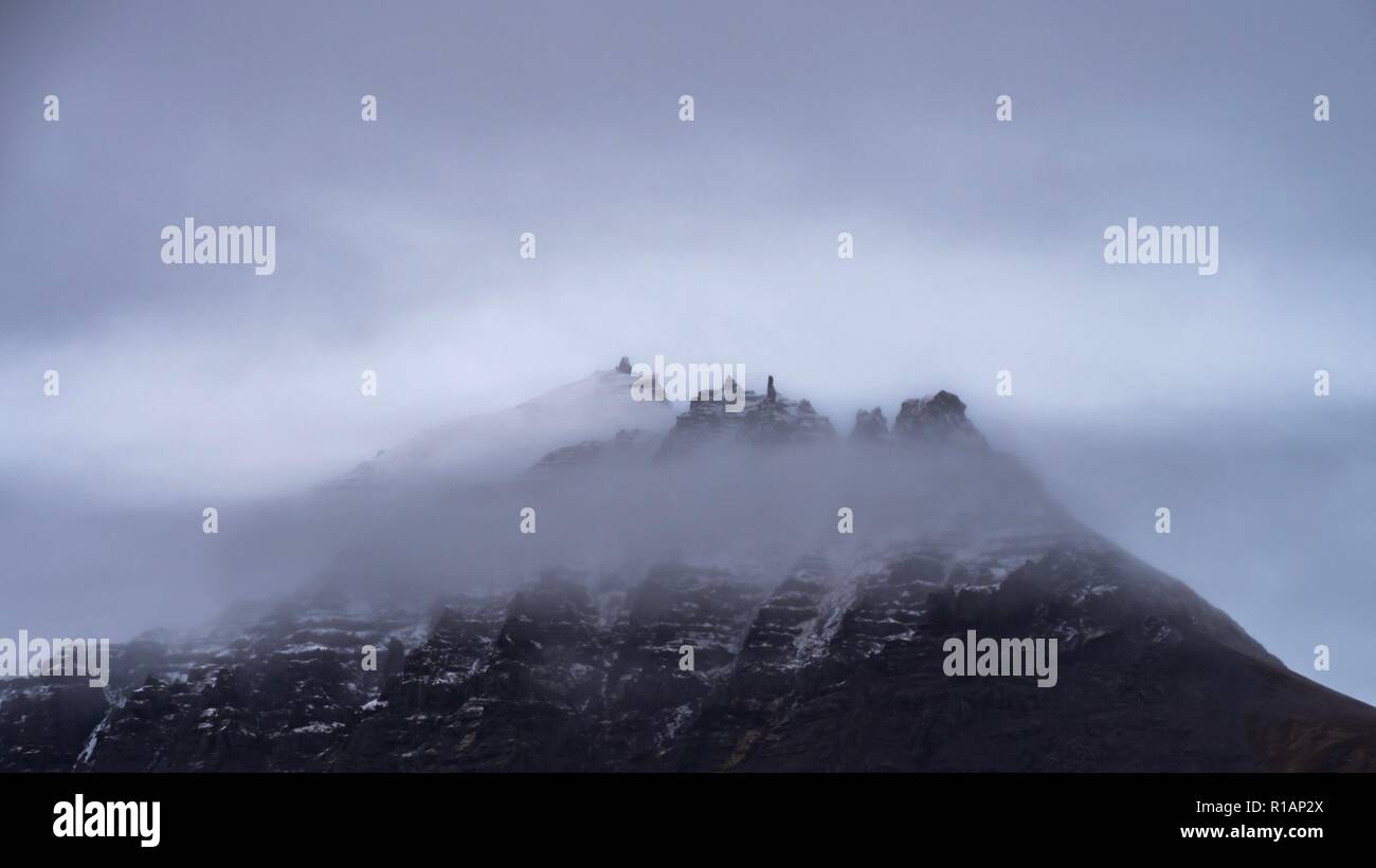 Die Spitzen der Berge durch die Wolke im südlichen Island erscheinen Stockfoto