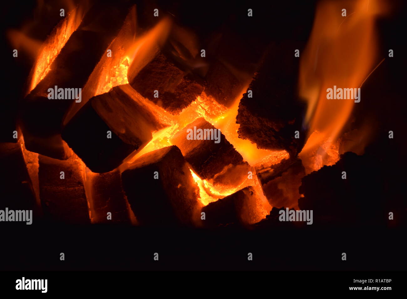 Nahaufnahme von Braunkohlenbriketts auf Feuer mit rot gelb Flammen in einer speziellen festen Ofen, rot und orange unscharfe Textur auf einem schwarzen Hintergrund. Stockfoto