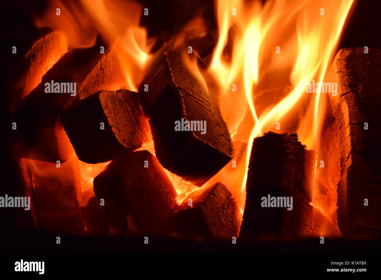 Nahaufnahme von Braunkohlenbriketts auf Feuer mit rot gelb Flammen in einer speziellen festen Ofen, rot und orange unscharfe Textur auf einem schwarzen Hintergrund. Stockfoto