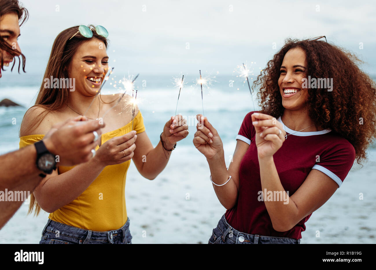 Multi-ethnischen Gruppe der jungen Menschen mit Wunderkerzen am Strand. Gruppe von Männern und Frauen Spaß mit Wunderkerzen im Freien am Strand. Stockfoto